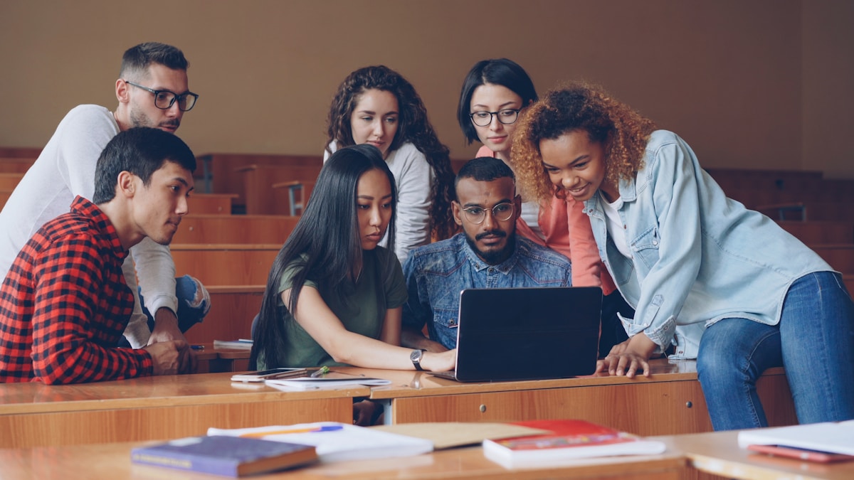 A diverse group of university students collaborating around a laptop in a lecture room